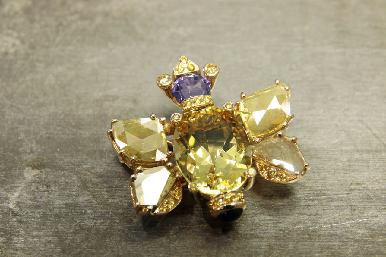 Brosche in Gelbgold / Weissgold 750 total 11.89 Gramm. Mit 1 Goldberyll 16 x 12 mm, 8.86 ct, 1 Saphir lavendel 6.26 x 5.64 x 4.86 1.54 ct (not heat), 2 Diamant Scheiben yellow total 0.56 ct, 2 Diamant Scheiben yellow total 1.22 ct, 1 Saphir blau Cabochon 0.56 ct und 29 Brillanten fancy yellow Si – I1, total 0.43 ct.